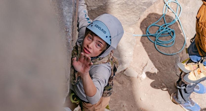 A person wearing safety gear is secured by ropes as they climb a rock wall. 